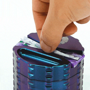 Hand placing rolling paper into the unique blue/purple Planet Burple Grinder, showcasing its vibrant design.
